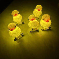 Five small glowing duck-shaped night lights with warm yellow bodies and orange beaks, arranged on a dark surface.