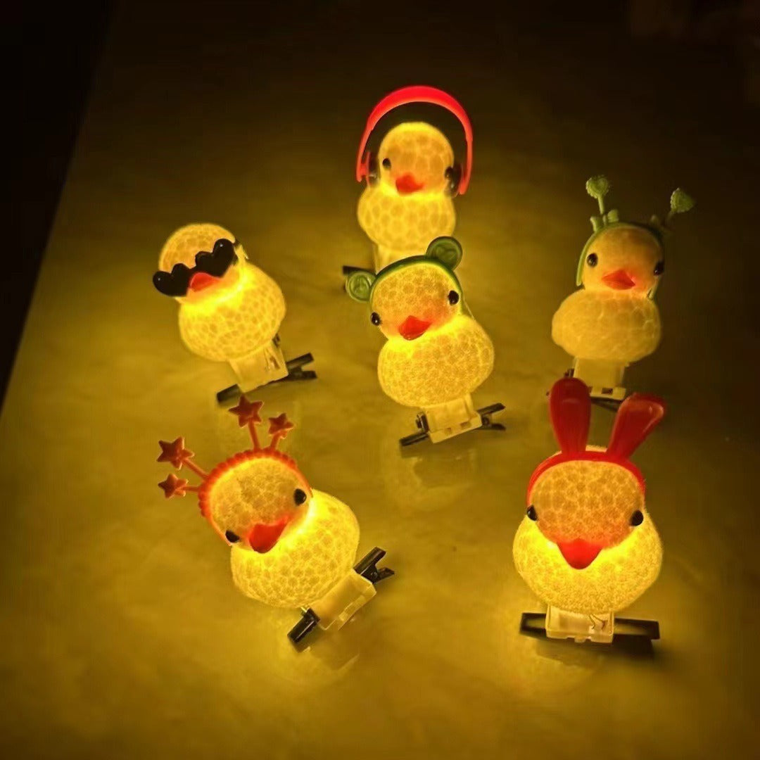 Six small duck-shaped night lights with different colorful winter hats and accessories, glowing with a warm yellow light on a dark surface.