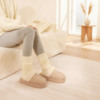 Person wearing beige slippers and gray leggings sitting on a couch.