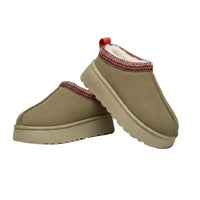 A pair of slip-on winter boots in a muted taupe-beige suede-like material, featuring a red and white patterned trim around the collar and a small red pull tab, photographed on a white faux-fur surface.