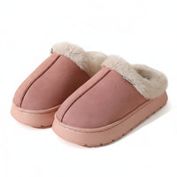 A pair of dusty pink slip-on slippers with fluffy white faux-fur trim, shown on a warm beige background.