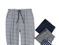 Gray and white striped lounge pants laid flat on a white background, styled with folded navy, gray, and striped pants, plus printed papers and a small white frame.
