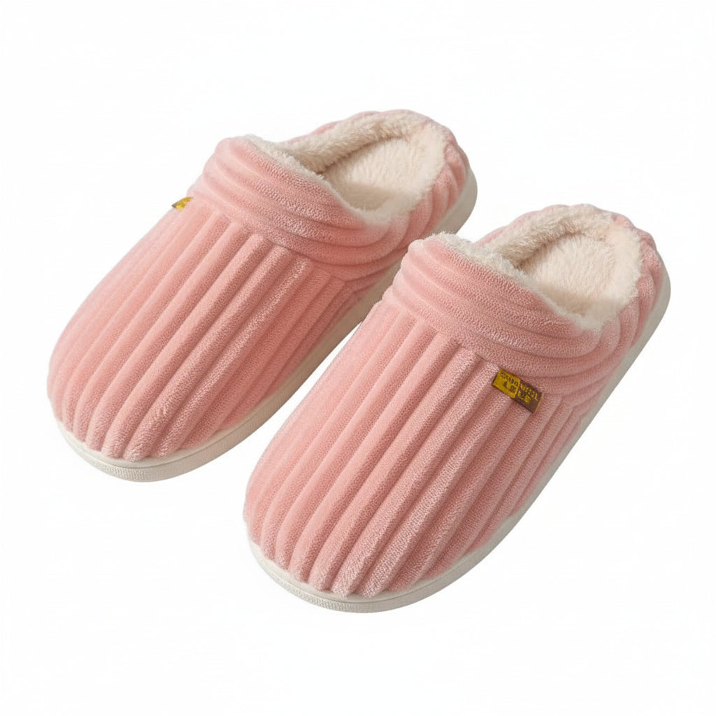 Pink slippers with a textured sole held by a person against a brown background