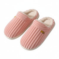 Pink slippers with a textured sole held by a person against a brown background