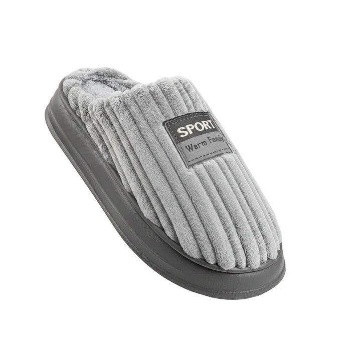 A gray ribbed fleece slipper with a dark gray sole, held in a hand against a white background. The slipper features a black label with the text 'SPORT Warm Family'.