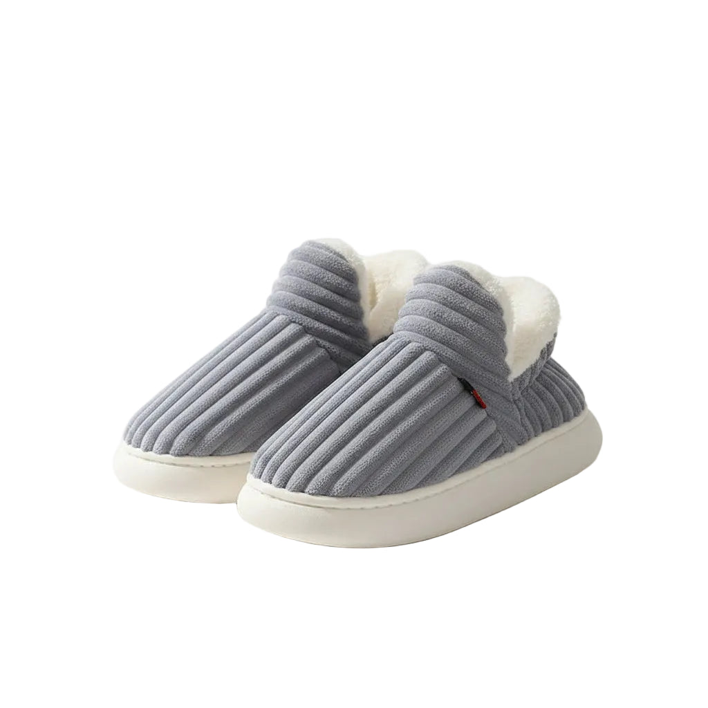 A pair of gray ribbed slip-on house slippers with white sherpa lining, resting on a beige surface.