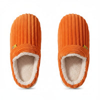 Orange slippers with a brand label held by a hand against a brown background