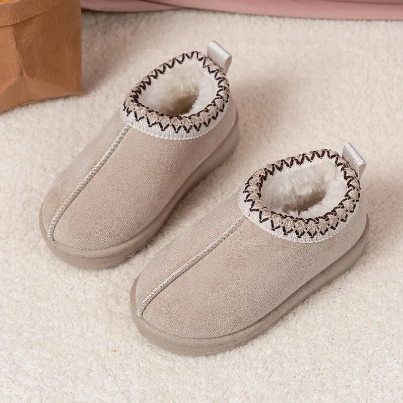 A pair of beige slip-on slippers with a soft white faux-fur lining and a decorative zigzag trim around the collar, displayed on a textured cream carpet.