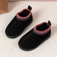 A pair of black slip-on winter boots with a soft fuzzy lining and a red, white, and black patterned trim around the collar, resting on a light beige textured surface.
