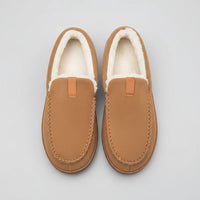 Pair of brown slippers with white fur lining on a wooden floor.