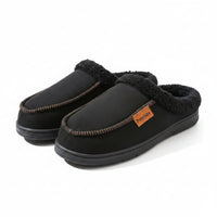 A pair of black slip-on winter slippers with a plush dark gray fleece lining and decorative stitching, resting on a wooden surface next to a blue storage box.