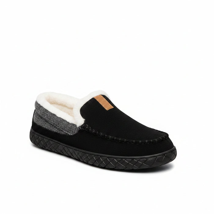 A pair of black slip-on slippers with white sherpa lining, a gray knit heel panel, and a small tan leather accent tab, shown on a light gray background.