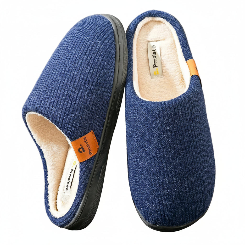 A pair of blue knit slip-on house slippers with a cream-colored fleece lining and a small orange brand tab, shown on a neutral beige background.