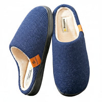 A pair of blue knit slip-on house slippers with a cream-colored fleece lining and a small orange brand tab, shown on a neutral beige background.