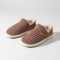 Brown slippers with white soles worn by a person on a brown background