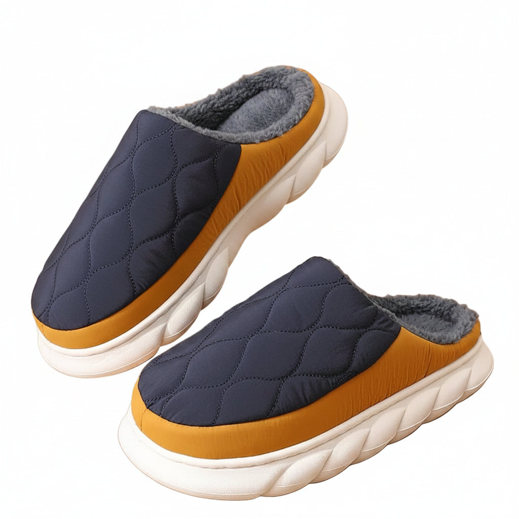 Pair of quilted slippers with brown soles and gray tops on a wooden floor.