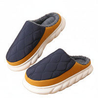 Pair of quilted slippers with brown soles and gray tops on a wooden floor.
