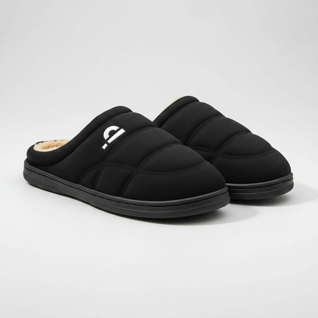 Black slippers with beige lining on a wooden floor, featuring the brand 'Pmoiste'.