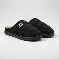 Black slippers with beige lining on a wooden floor, featuring the brand 'Pmoiste'.