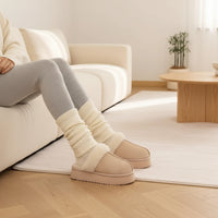 Beige slippers with white ribbed cuffs worn indoors on a light-colored carpet.