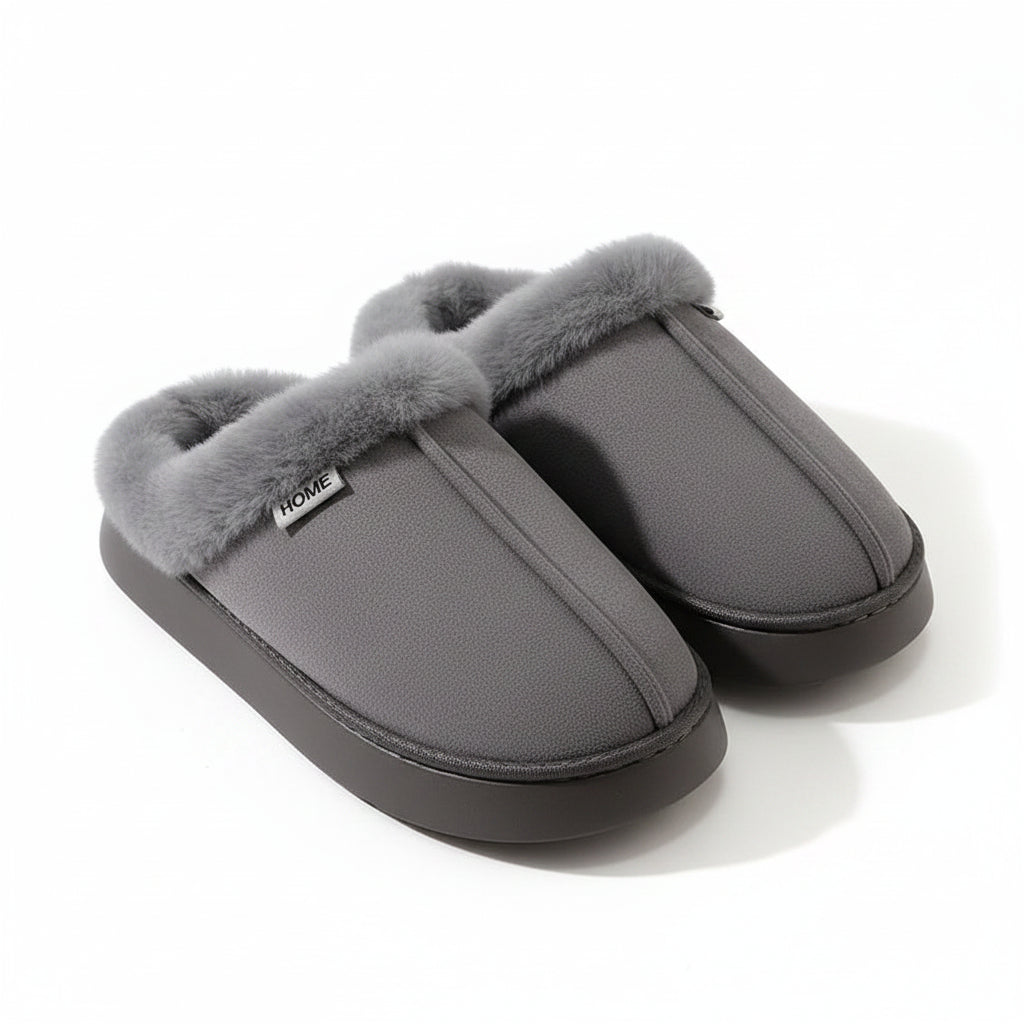A pair of gray slip-on house slippers with fluffy faux-fur trim and a dark sole, displayed on a beige surface with a white textured blanket in the background.