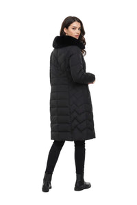 A woman modeling a long black quilted puffer coat with a black faux-fur collar, shown from a three-quarters back view against a plain white studio background.