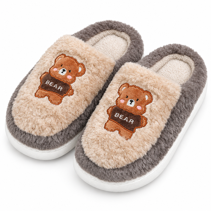 A pair of plush slip-on house slippers with a beige sherpa upper, gray trim, and a brown embroidered teddy bear holding a sign that says 'BEAR' on the front, shown on a white background.