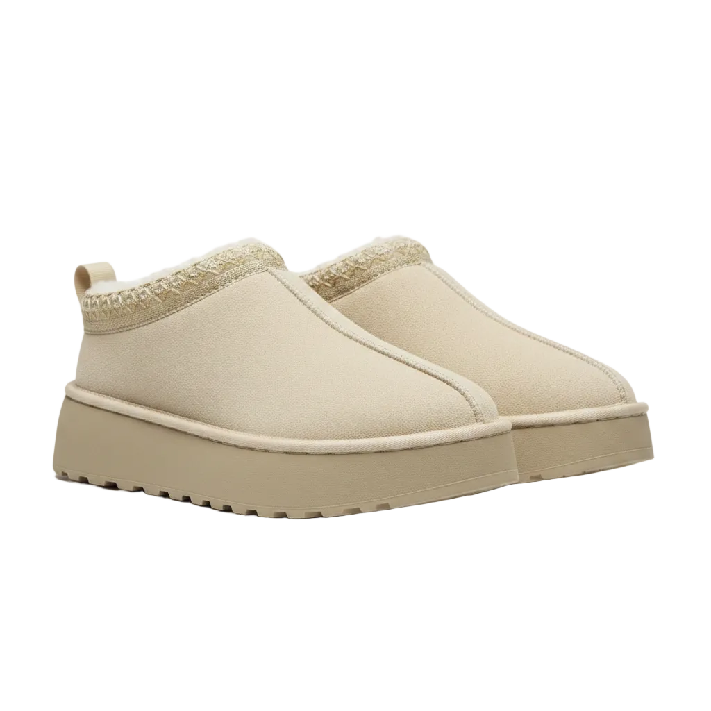 A pair of slip-on platform mule slippers in a warm cream or beige color, featuring a textured knit trim around the opening and a thick lug sole, shown against a plain white background.