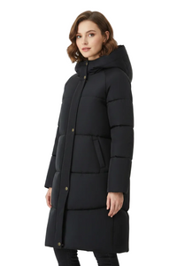 A woman modeling a long black puffer coat with a hood and gold-tone snap buttons, photographed against a plain white studio background.