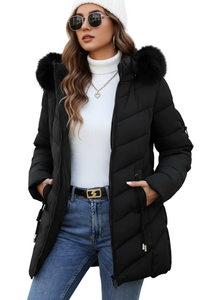 A woman wearing a black puffer jacket with a fur-trimmed hood, a white ribbed turtleneck, blue jeans, sunglasses, and a white beanie, posed against a plain white background.