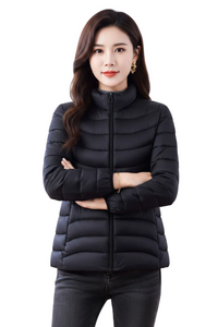 A woman modeling a black puffer jacket with a high collar and front zipper, paired with dark gray jeans, against a plain white background.