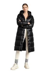 A model stands in a studio wearing a long black puffer coat over cream leggings, gray socks, and cream sneakers.
