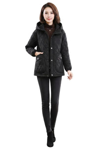 A woman modeling a black quilted winter jacket with a hood, front zipper, and snap buttons, paired with black leggings and black ankle boots, against a plain white background.