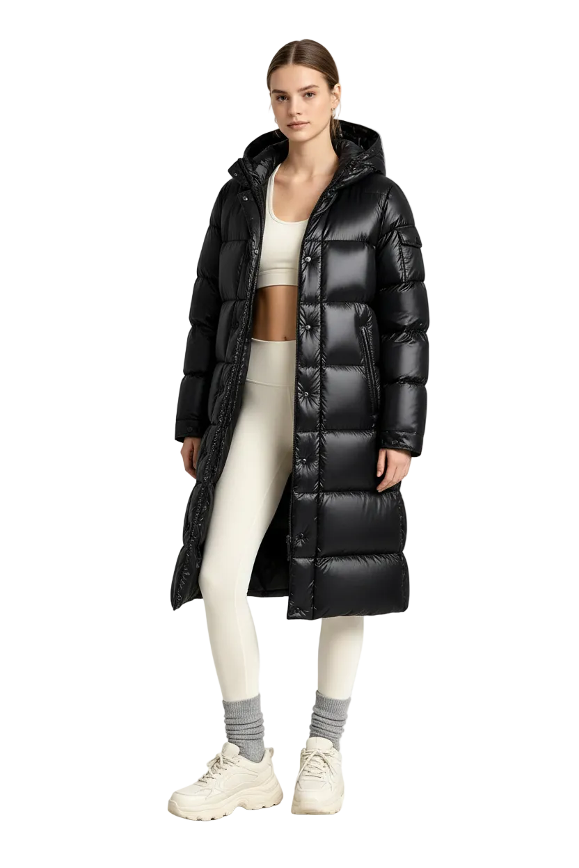A model stands in a studio wearing a long black puffer coat over a cream sports bra and leggings, paired with gray socks and off-white sneakers.
