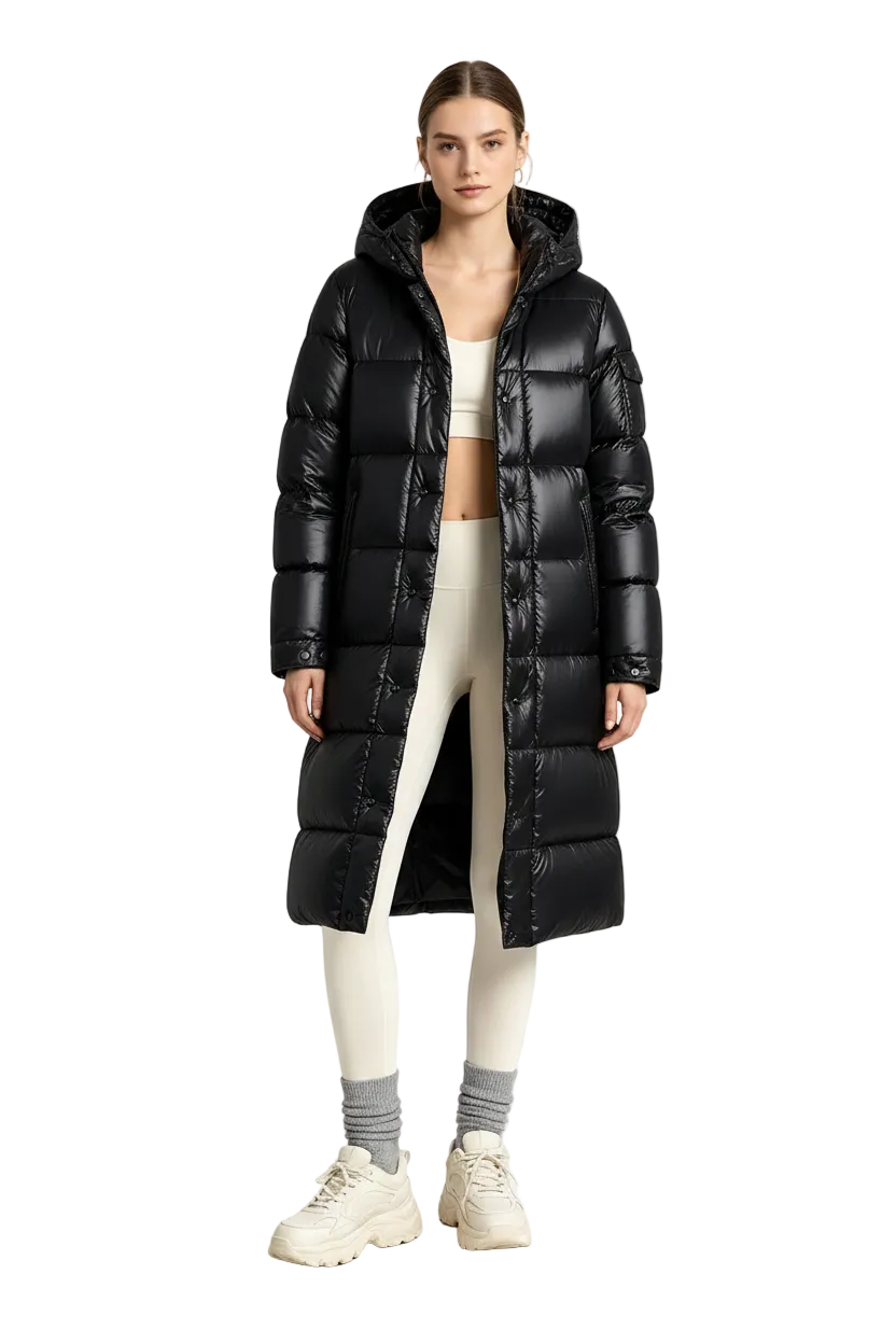 A model stands in a studio wearing a long black puffer coat over a white crop top, white leggings, gray socks, and white sneakers.