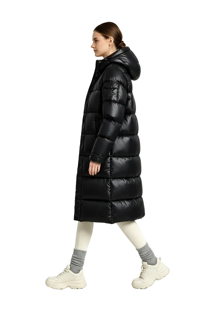 A woman modeling a long black puffer coat in a studio setting. She is shown in profile walking, wearing cream leggings, gray socks, and chunky off-white sneakers.