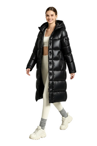 A woman models a long black puffer coat in a bright studio setting. She is wearing a beige sports bra, beige leggings, gray socks, and chunky off-white sneakers.