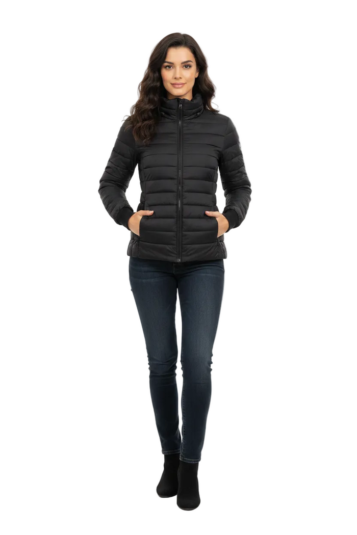 A woman modeling a black puffer jacket with a high collar and front zipper, paired with dark blue skinny jeans and black ankle boots, against a plain white studio background.