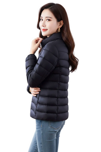 A woman wearing a black quilted puffer jacket and blue jeans, photographed against a plain white studio background.