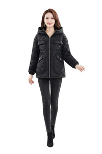 A woman modeling a black quilted hooded puffer jacket with a front zipper and flap pockets, paired with black skinny pants and black ankle boots, against a plain white studio background.