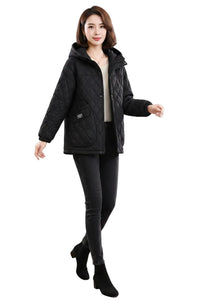 A woman modeling a black quilted hooded puffer jacket, styled with a beige top, black skinny pants, and black ankle boots, against a plain white background.