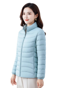 A woman wearing a light blue puffer jacket with a high collar and front zipper, paired with light beige pants, photographed against a clean white studio background.