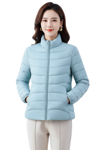 A woman wearing a light blue puffer jacket with a high collar and front zipper, paired with light beige pants, set against a plain white background.
