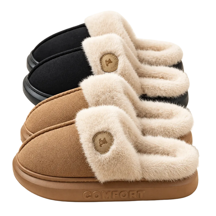 Three pairs of slip-on plush slippers arranged in front of each other on a light cream background. The front pair is tan with a cream faux-fur trim and a tan circular logo patch; the middle pair is taupe; the back pair is black.