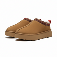 A pair of slip-on platform mule shoes in tan canvas, featuring a patterned trim around the collar and a red pull tab on the heel, set against a plain white background.