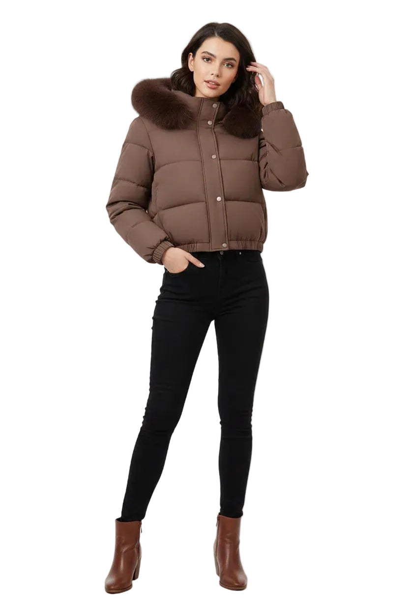 A woman modeling a cropped brown puffer jacket with a dark brown faux-fur collar, paired with black skinny pants and brown ankle boots, against a plain white studio background.