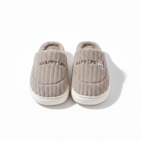 A pair of light taupe ribbed slip-on slippers with white soles, featuring 'HAPPY LIFE' embroidered on the side and a small cartoon bunny face on the right slipper.