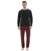 A man wearing a black long-sleeve shirt and red and black plaid pajama pants, standing against a plain white background.