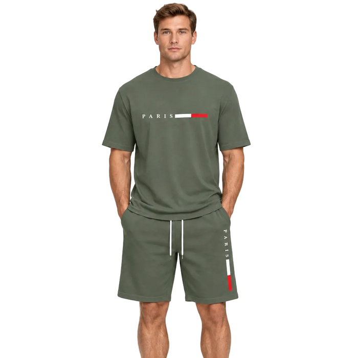 A man modeling an olive green matching lounge set consisting of a short-sleeve t-shirt and shorts. The t-shirt features 'PARIS' printed in white next to a white and red stripe logo, while the shorts have white drawstrings and a vertical white and red 'PARIS' print on the side.