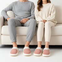 A man and a woman sitting side by side on a cream-colored couch, wearing matching cozy knit loungewear sets. The man wears a light gray long-sleeve top and jogger pants, while the woman wears a cream knit sweater and matching cream leggings.